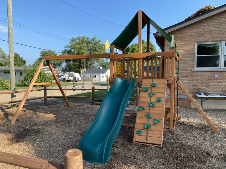 Wooden play structure with a green slide on the masjid grounds beside the building